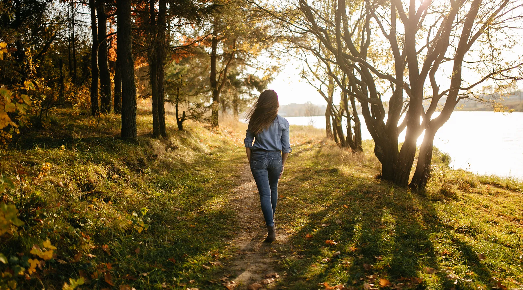 Young woman walking between autumn trees beside a lake