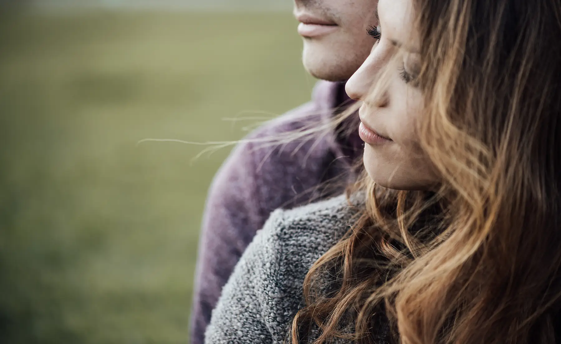 A contented young couple sitting together with a green grassy background
