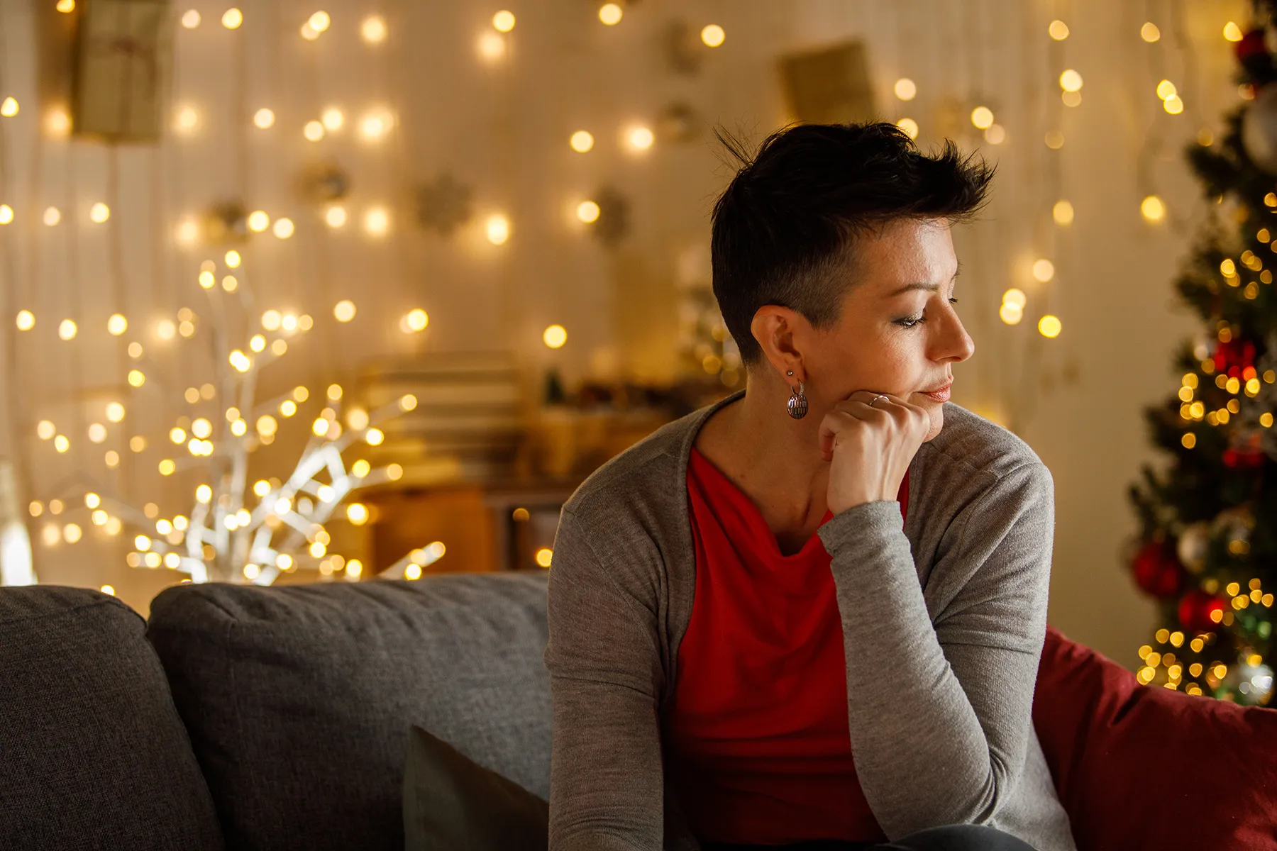 Woman sitting on a lounge by herself looking to the side with Christmas decorations in the background